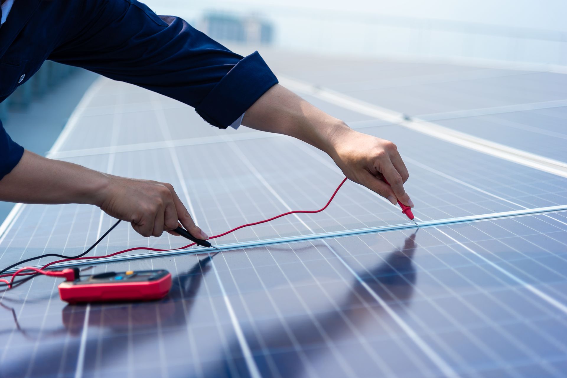 Un technicien utilise un multimètre pour tester la tension électrique des panneaux solaires sur un toit.