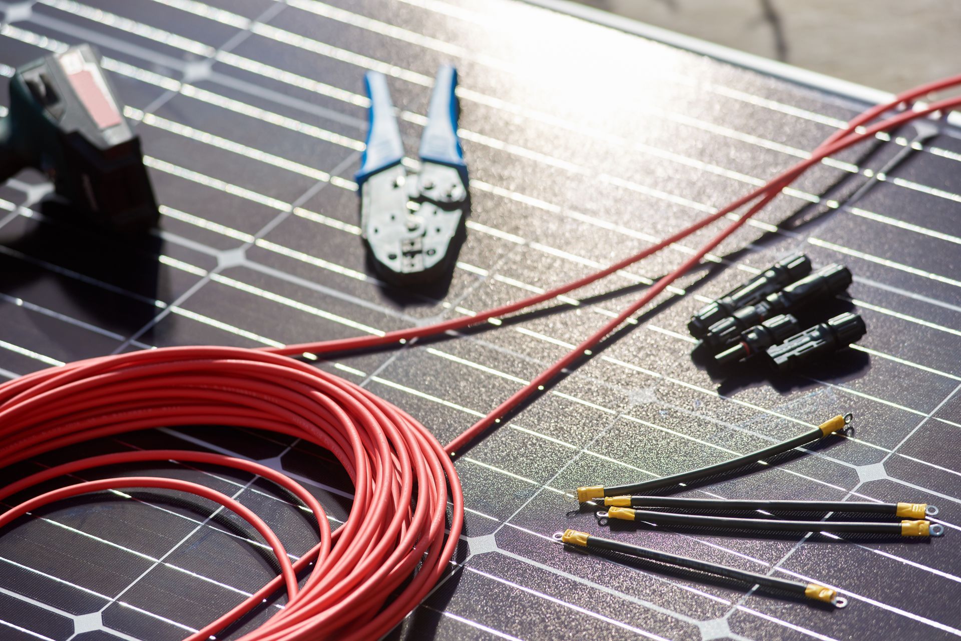 Outils et fil rouge pour l'installation de panneaux solaires, y compris une pince à sertir, des connecteurs et un câble sur la surface d'un panneau solaire.