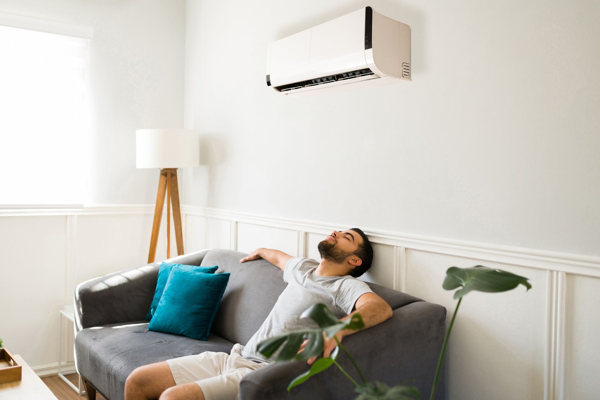 Une personne se détend sur un canapé gris sous un climatiseur dans un salon moderne et lumineux.