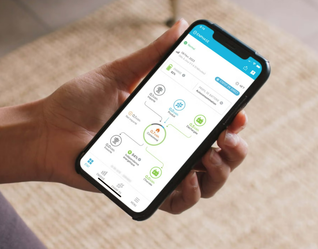 Une personne tient un smartphone affichant le tableau de bord d'une application de gestion d'énergie propre avec des icônes représentant l'énergie solaire, les batteries et la consommation domestique.