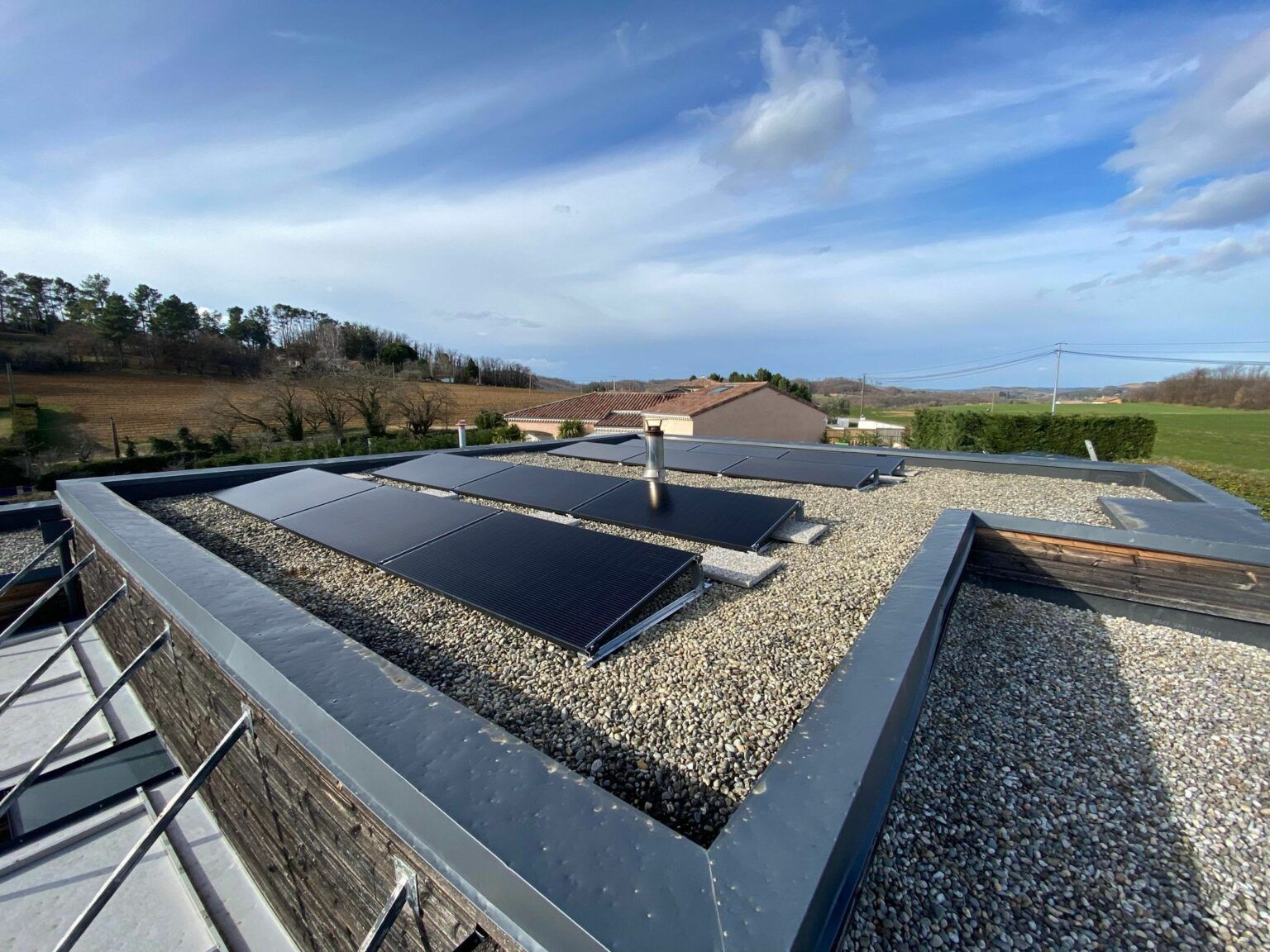 Des panneaux solaires installés sur un toit plat recouvert de gravier, sous un ciel bleu légèrement nuageux.
