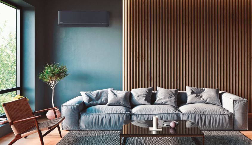 Dans un salon élégant, un canapé gris est placé devant un mur à lattes de bois, à côté d'une chaise moderne et d'une petite plante en pot.