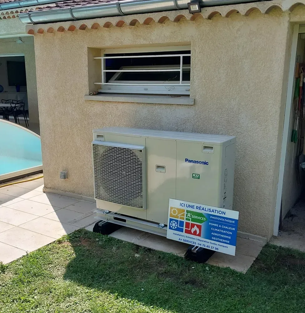 Une pompe à chaleur Panasonic beige est installée à l'extérieur d'une maison, sur des supports noirs, près d'une pelouse et d'une petite piscine.