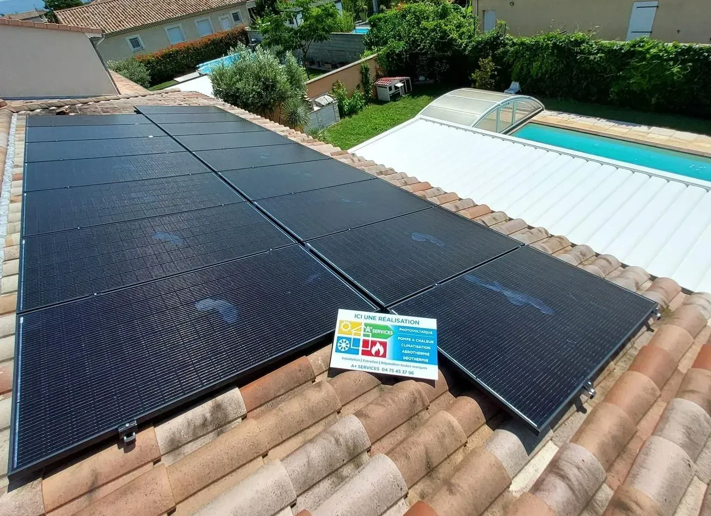 Des panneaux solaires thermiques sont installés sur un toit en tuiles de terre cuite, situé à côté d'une piscine dans un jardin résidentiel.