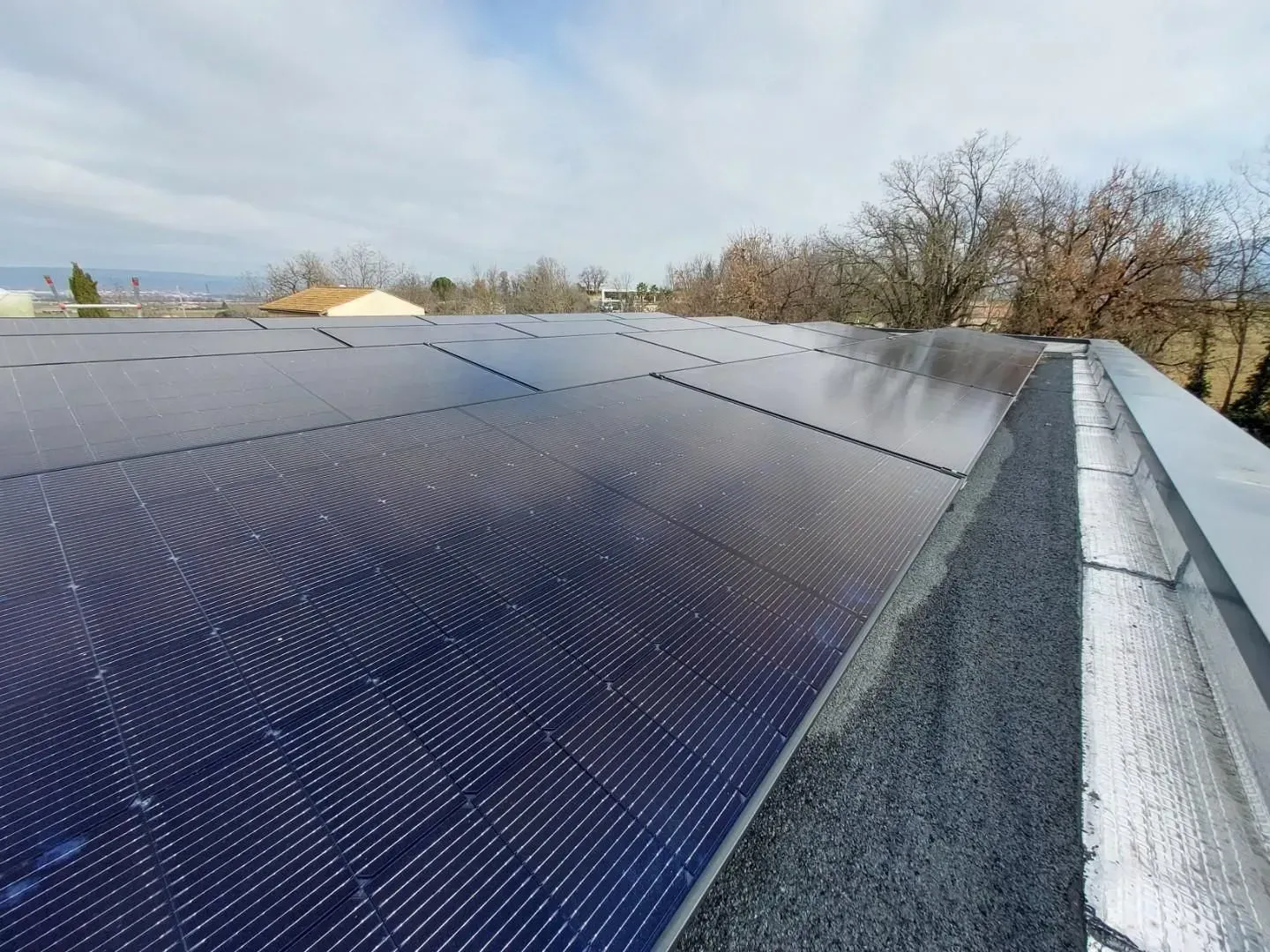 Des panneaux solaires disposés en rangées sur un toit plat recouvert de gravier, sous un ciel partiellement nuageux.