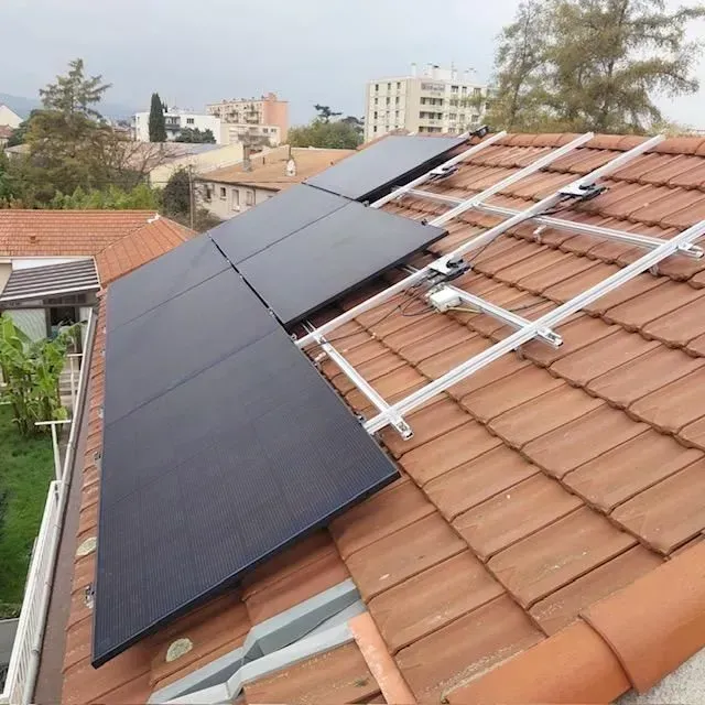 Trois panneaux solaires noirs sont montés sur un toit en tuiles de terre cuite d'une maison, avec une structure métallique inachevée visible.