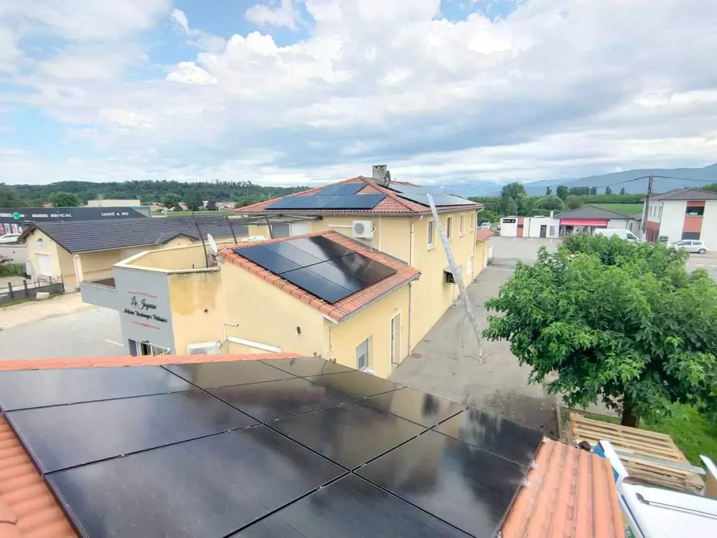 Vue depuis les toits montrant plusieurs bâtiments équipés de panneaux solaires noirs sous un ciel partiellement nuageux.