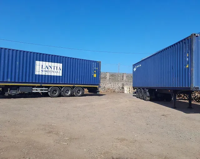 Dos contenedores de envío azules están estacionados uno al lado del otro.