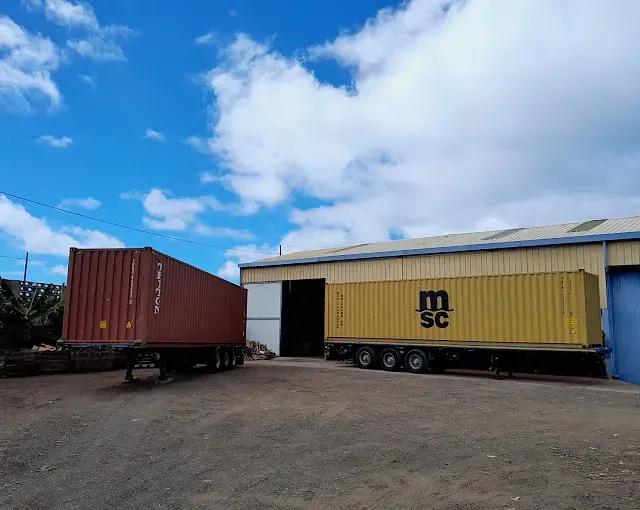 Dos contenedores de envío están estacionados frente a un edificio.