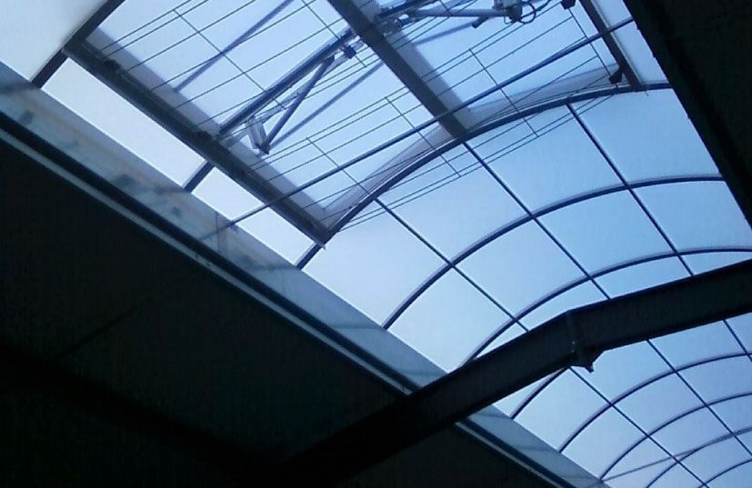 Vue sur le ciel bleu à travers une grille de panneaux de verre cintrée et rectangulaire soutenue par des poutres métalliques.