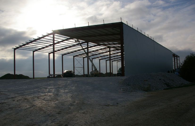 Bâtiment à ossature métallique en construction, vue extérieure avec la lumière du soleil filtrant à travers la structure.