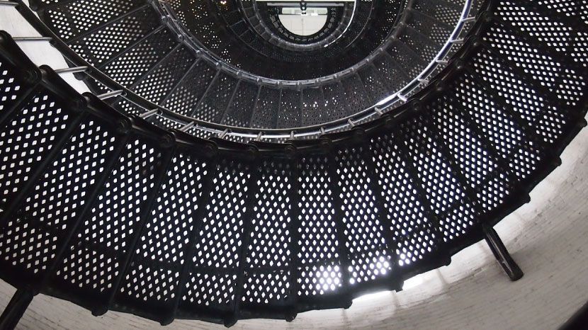 En regardant un escalier en colimaçon aux marches en métal noir et aux murs blancs.