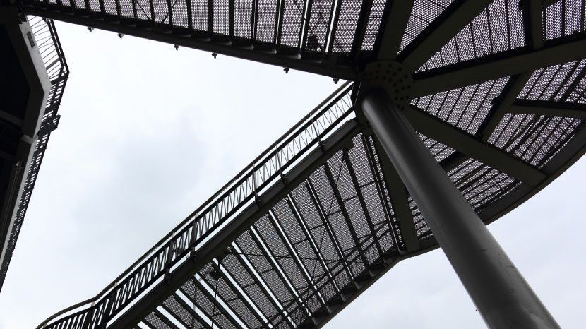 Vue en contre-plongée d'une passerelle métallique sur fond de ciel nuageux.