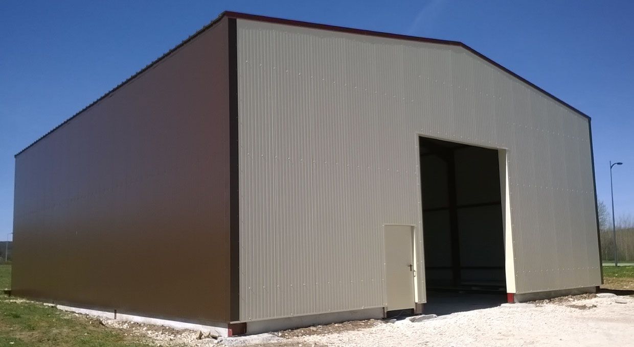 Grand bâtiment de stockage en métal beige avec porte ouverte, se détachant sur un ciel bleu.
