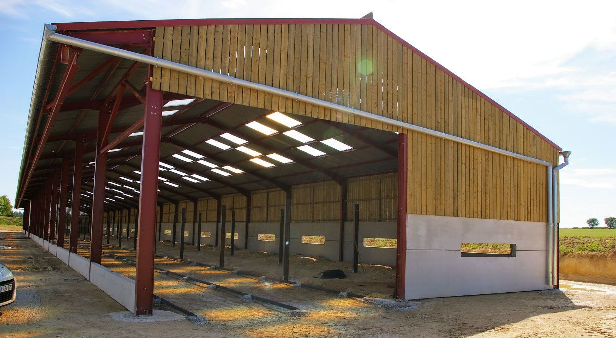 Grange à ossature métallique et bardage en bois en construction, avec un côté ouvert, sur fond de ciel bleu.
