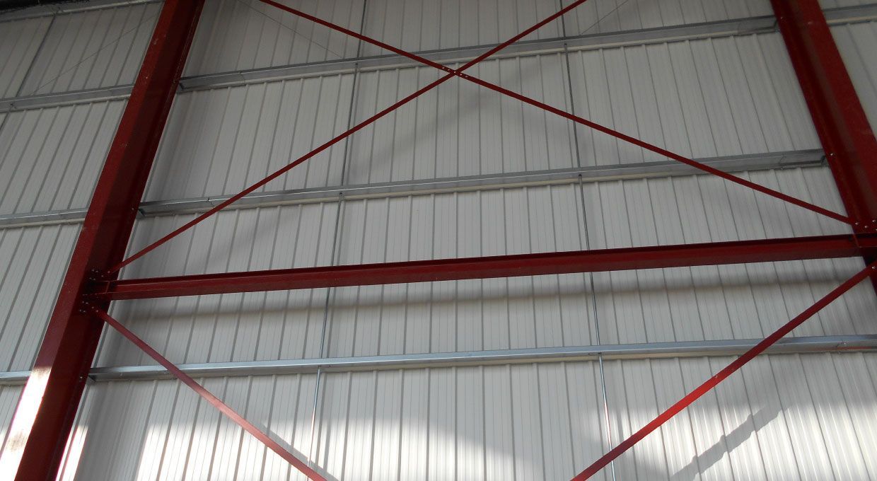 Cadre en acier rouge avec contreventement contre un mur en métal blanc.