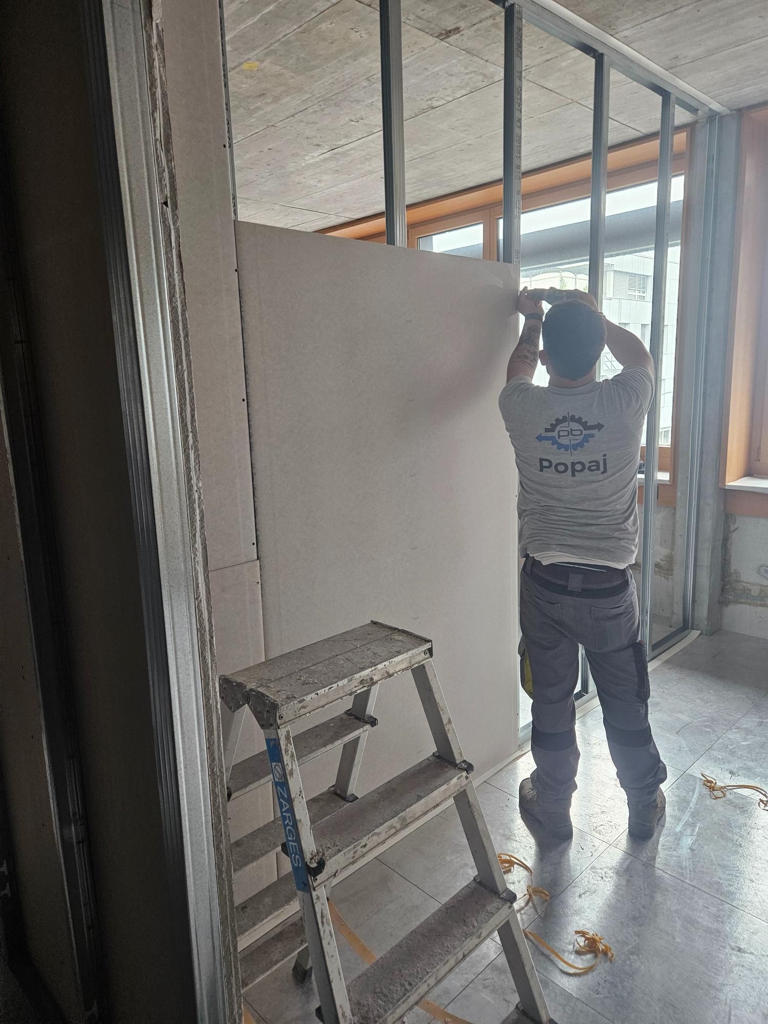 Ein Mann steht neben einer Leiter in einem Raum. Foto von der Popaj GmbH