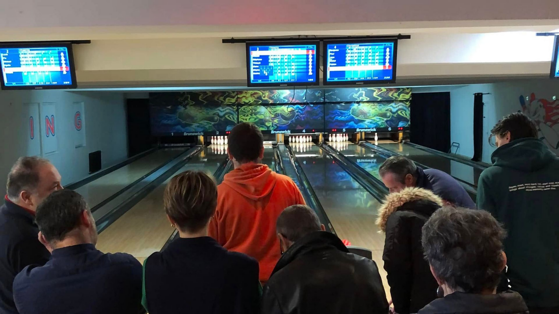 Des joueurs devant des pistes de bowling avec des écrans affichant leurs scores