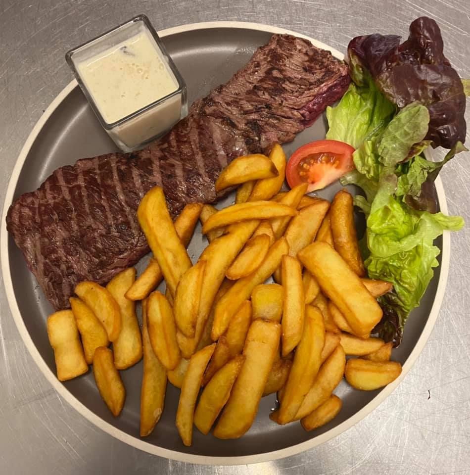 Steak avec frites, sauce, tomate et salade sur une assiette grise.