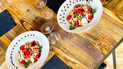 Deux salades de fruits dans des bols blancs sur une table en bois rustique avec des verres à vin.