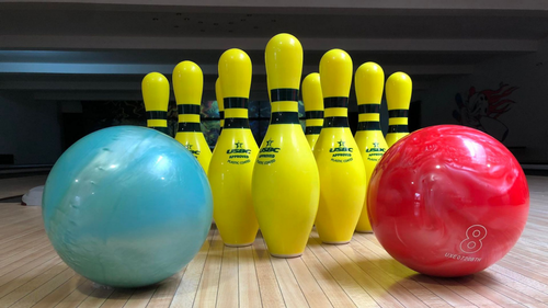 Deux boules de bowling (bleue, rouge) devant des quilles jaunes sur une piste.