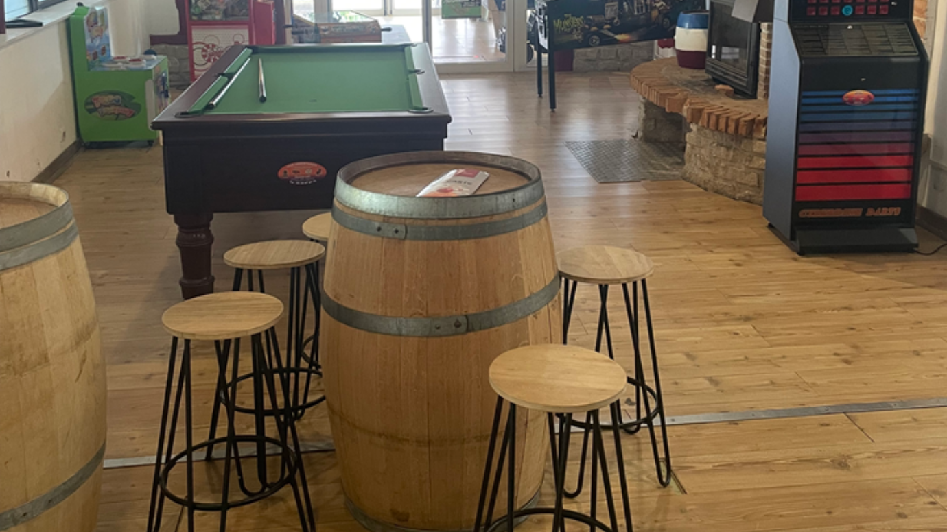 Table de billard, jeux d'arcade et tabourets de bar autour de barils dans une salle de jeux.
