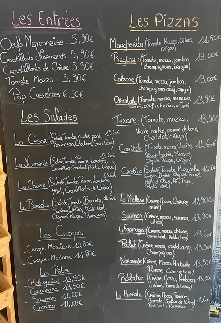 Menu sur tableau noir avec sélections et prix de plats écrits à la main.