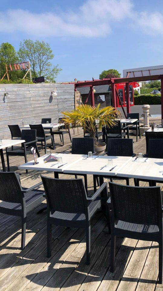 Terrasse de restaurant en plein air avec tables et chaises vides sous un ciel bleu vif.