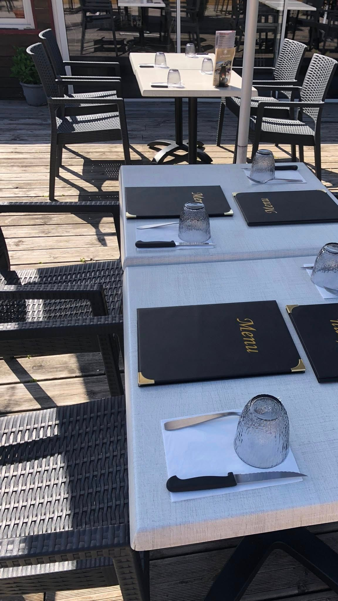 Tables de restaurant en plein air dressées avec menus, verres et couverts.