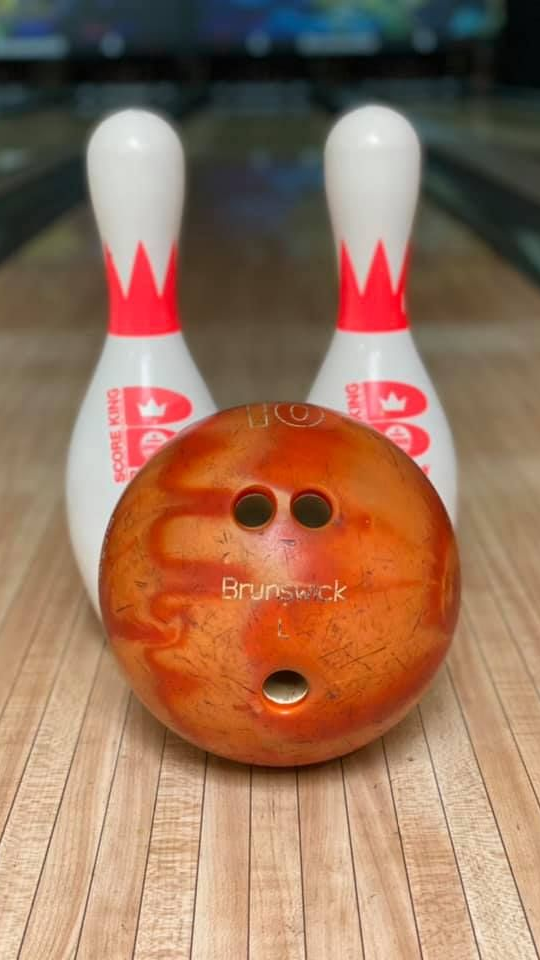 Boule de bowling devant deux quilles sur une piste en bois.