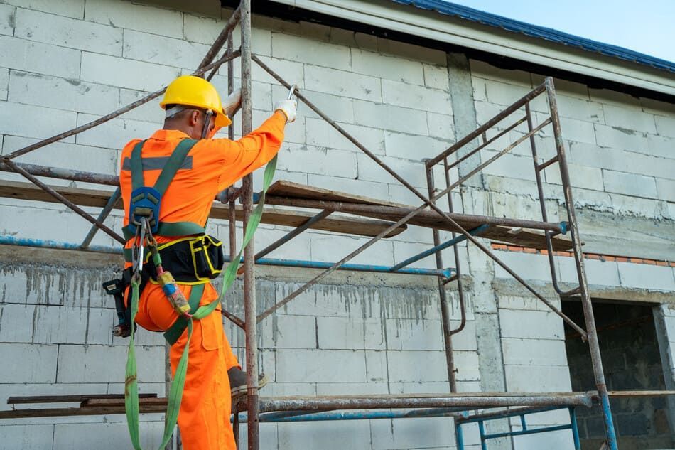 Un trabajador de la construcción está de pie en un andamio frente a un edificio.