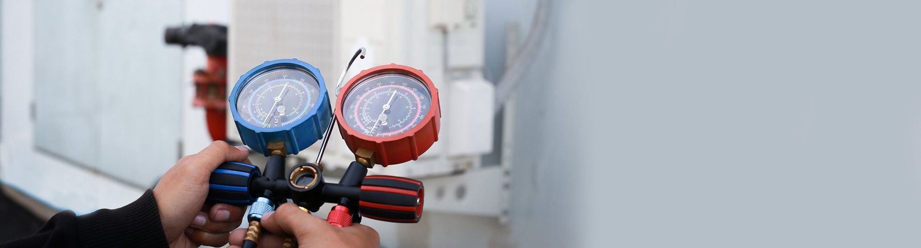 Manos sosteniendo un manómetro azul y rojo, probablemente probando un sistema de aire acondicionado.