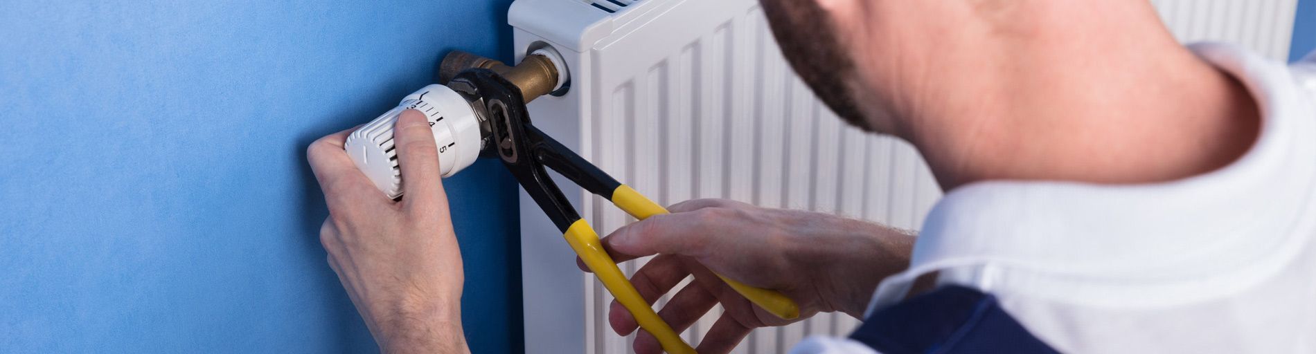 Una persona usa alicates para trabajar en un radiador cerca de una pared azul.
