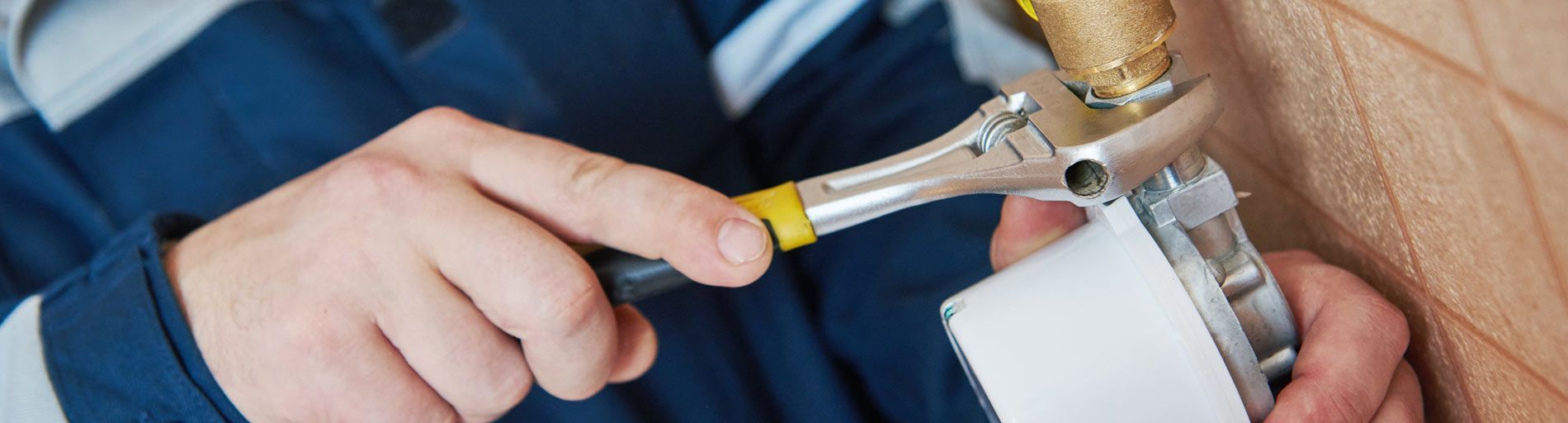 Una persona usa una llave inglesa para trabajar en un aparato blanco cerca de una tubería de cobre.
