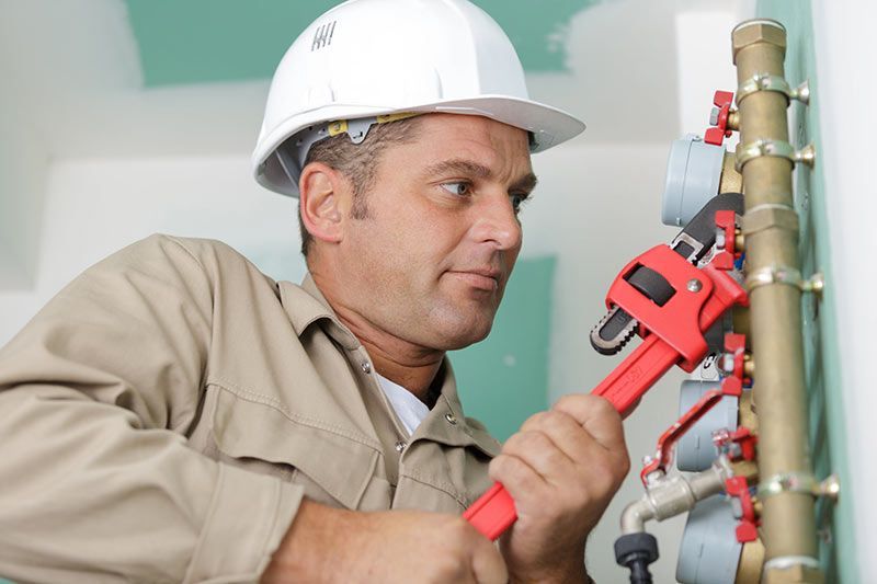 Fontanero con casco utilizando una llave inglesa en las tuberías.