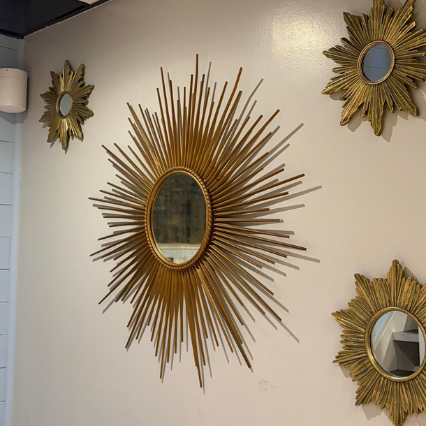 Miroirs dorés en forme de soleil sur un mur blanc, centrés autour d'un miroir rond