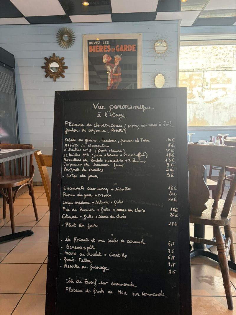 Menu de café noir sur un chevalet dans un restaurant rustique avec des chaises et une enseigne murale derrière.