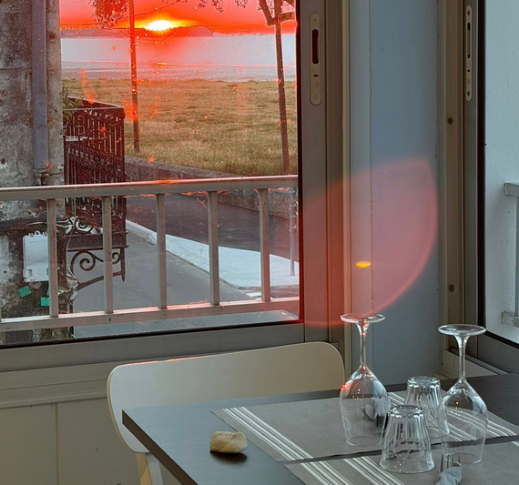 Table à manger baignée de soleil près d'une fenêtre au coucher du soleil, avec des verres et une vue sur la rue.
