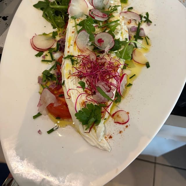 Poisson blanc servi avec des herbes, des radis, de la salade et une vinaigrette dans un plat ovale blanc.