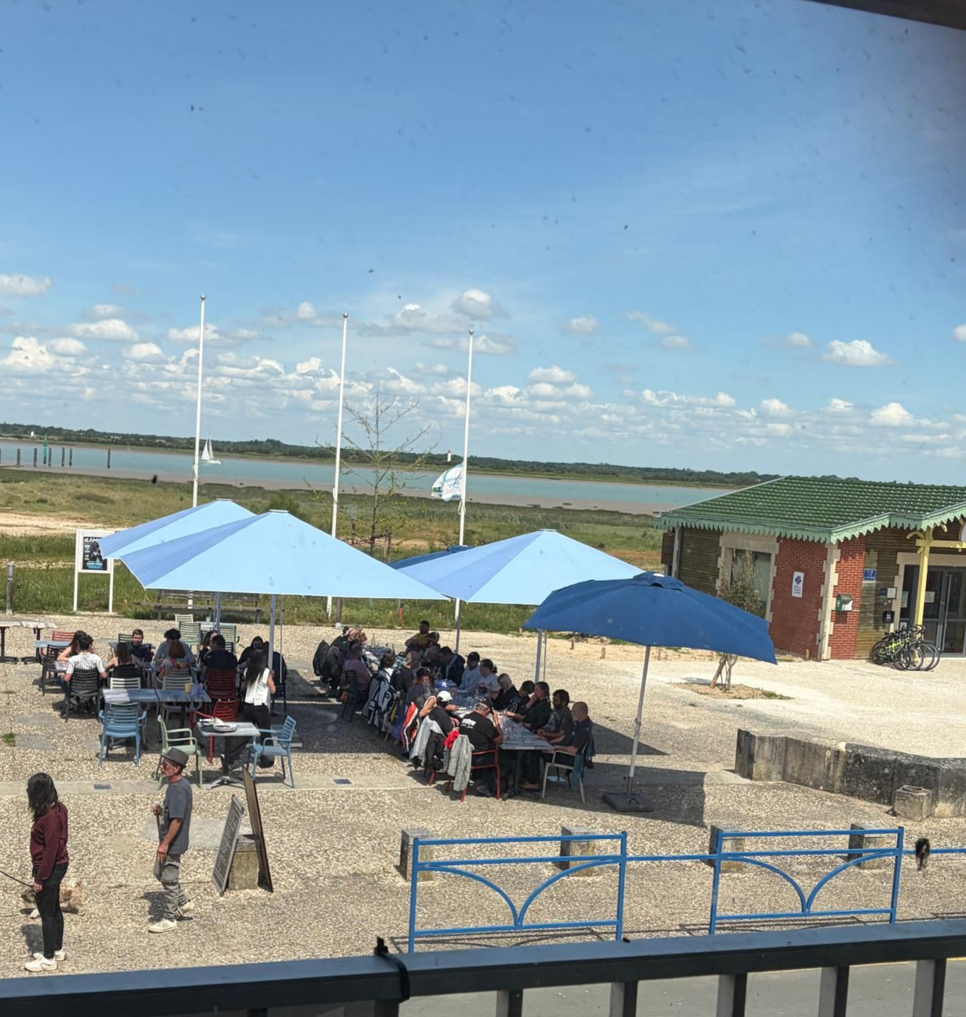 Terrasse du restaurant avec des personnes attablées en plein air sous des auvents bleus près du front de mer
