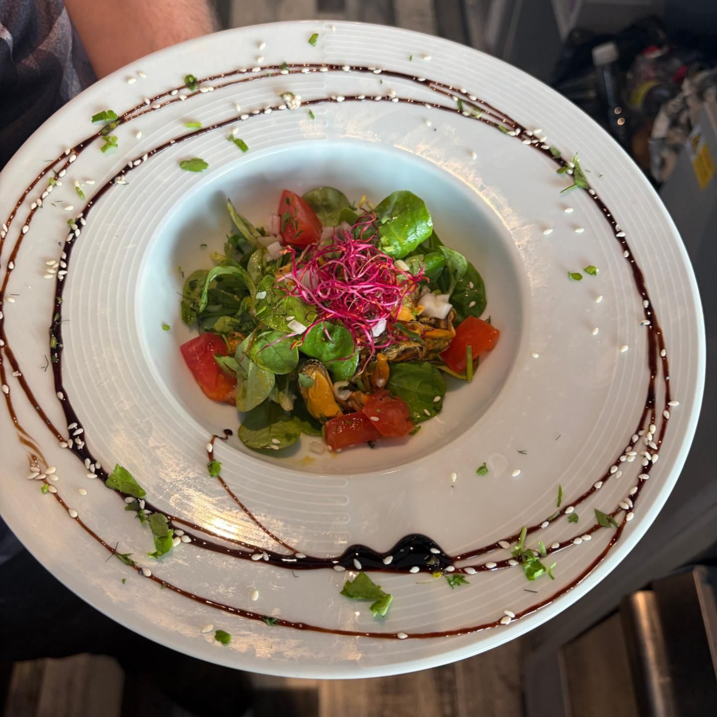 Salade gourmande composée de verdure, de tomates et d'une garniture rose, servie dans un bol blanc avec un filet de sauce foncée.