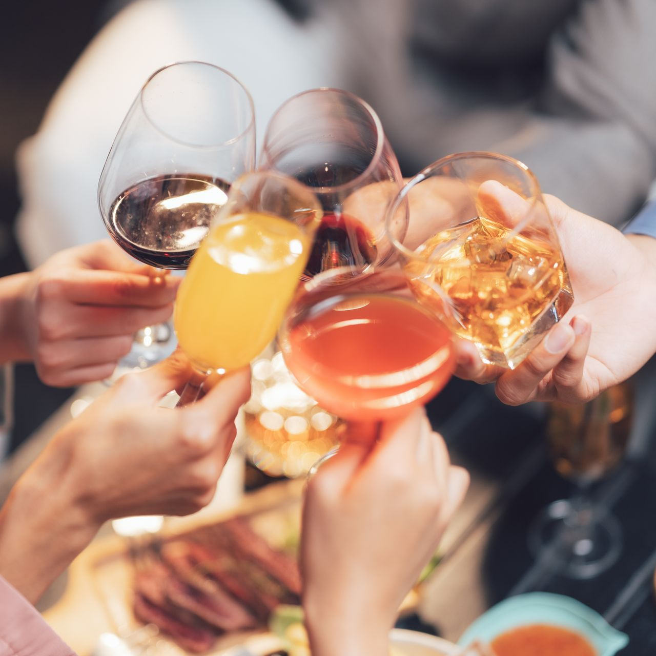 Des mains qui trinquent avec des cocktails colorés et des verres à vin lors d'une fête