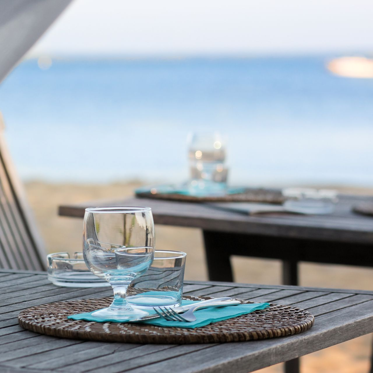 Verre et serviette pliée sur un set de table tissé, à une table en bord de mer avec l'océan bleu en arrière-plan.