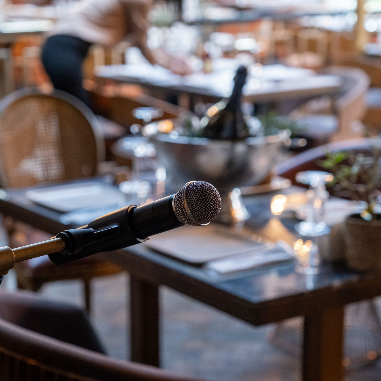 Un microphone posé sur une table dans la salle à manger chaleureuse d'un restaurant, avec des verres à vin et un seau à glace en arrière-plan.