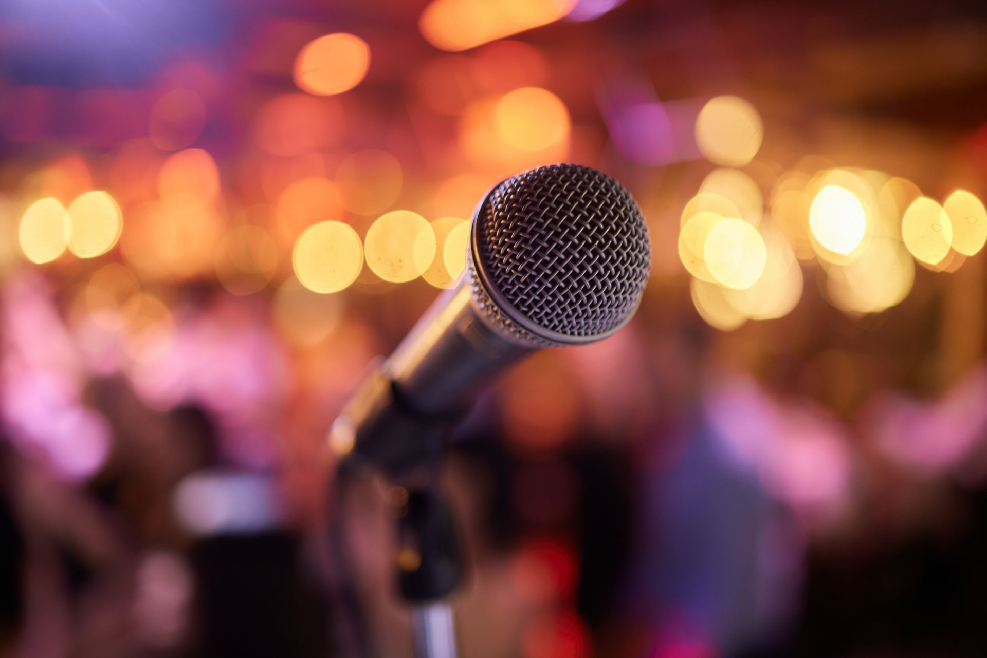 Un microphone sur pied au premier plan, avec en arrière-plan des lumières de scène chaudes et floues et la foule.
