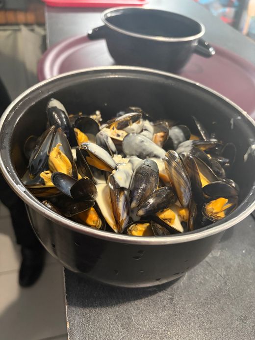 Un bol noir rempli de moules cuites est posé sur une table, avec un deuxième bol flou en arrière-plan.