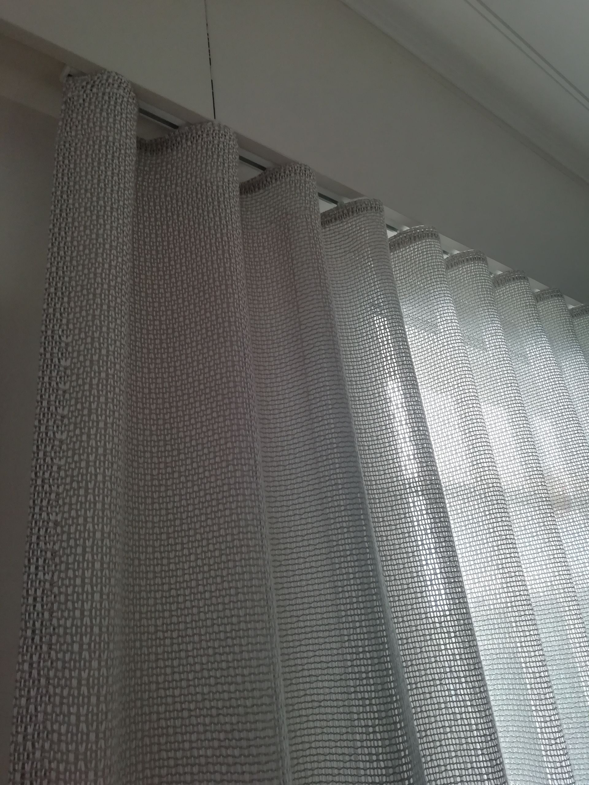 Des rideaux beiges transparents recouvrent une fenêtre, vus de l'intérieur de la pièce.