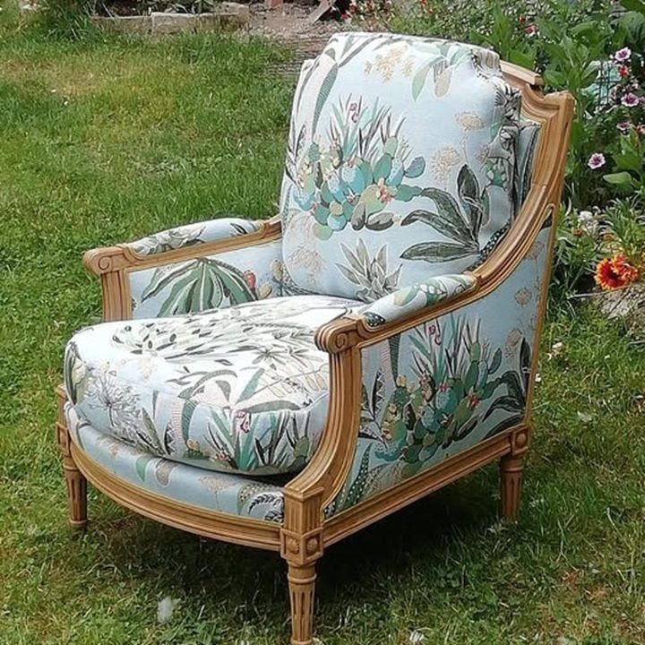 Un fauteuil à motif floral bleu clair, placé à l'extérieur sur l'herbe. La structure est en bois clair.
