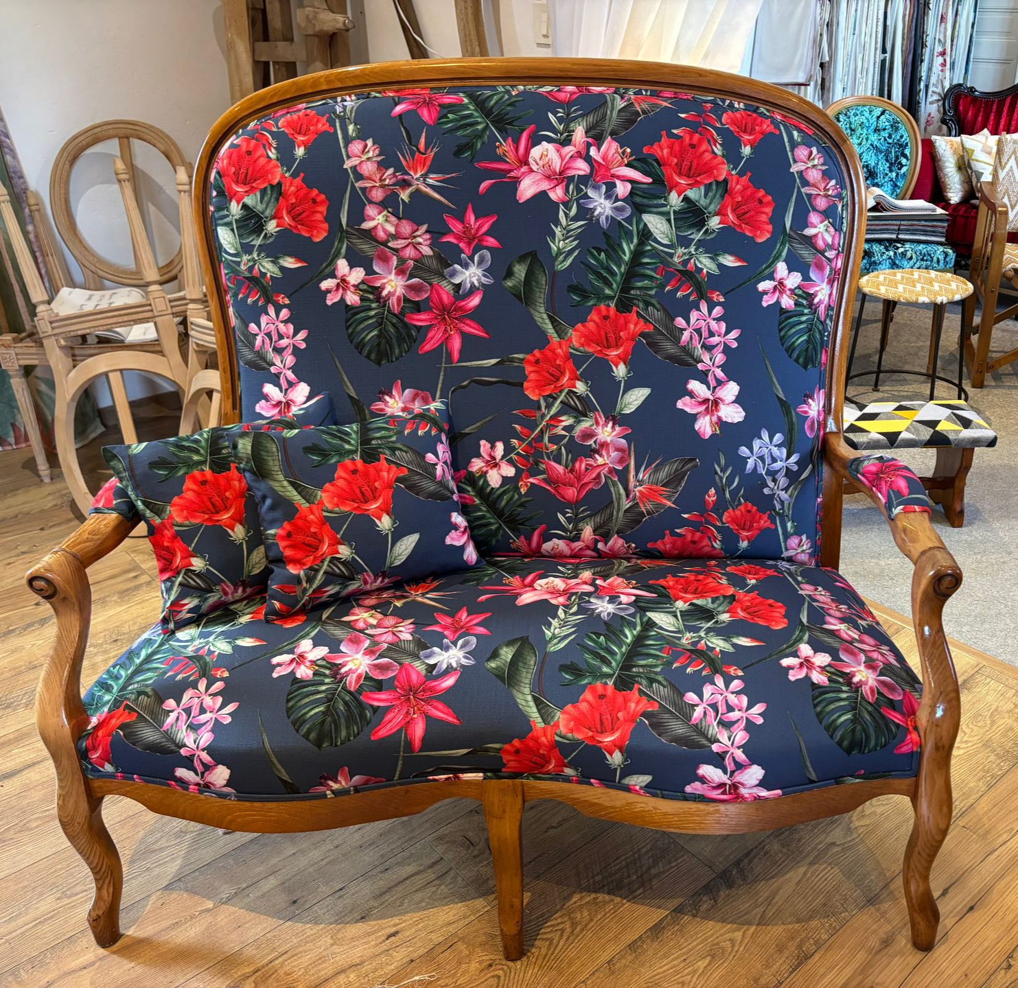 Canapé deux places ancien recouvert d'un tissu à motifs floraux, dans une pièce. Fleurs rouges et roses sur tissu bleu foncé, structure en bois.