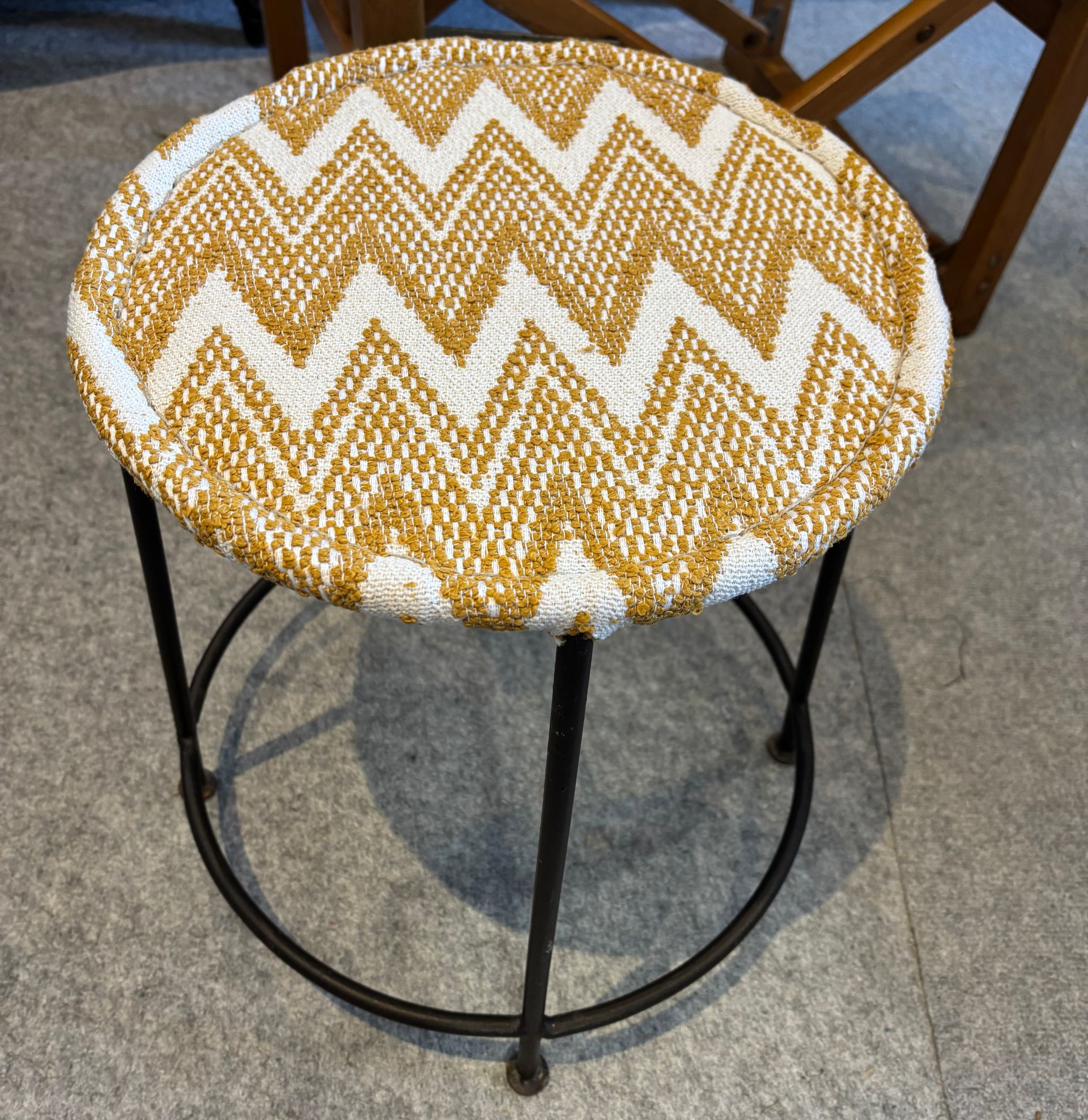 Tabouret rond avec assise à motifs en zigzag jaunes et blancs, pieds en métal noir.